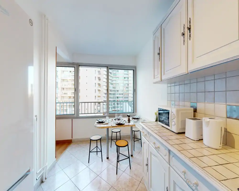 Cuisine lumineuse avec placards classiques, plans carrelés et un petit coin repas près d'une grande fenêtre — idéale pour des repas décontractés et une vue sur la ville.