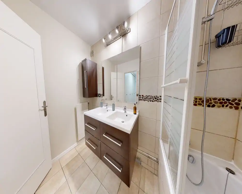 Salle de bains moderne avec meuble double vasque, grand miroir, carrelage mural et baignoire avec paroi de douche — lumineuse et soignée.