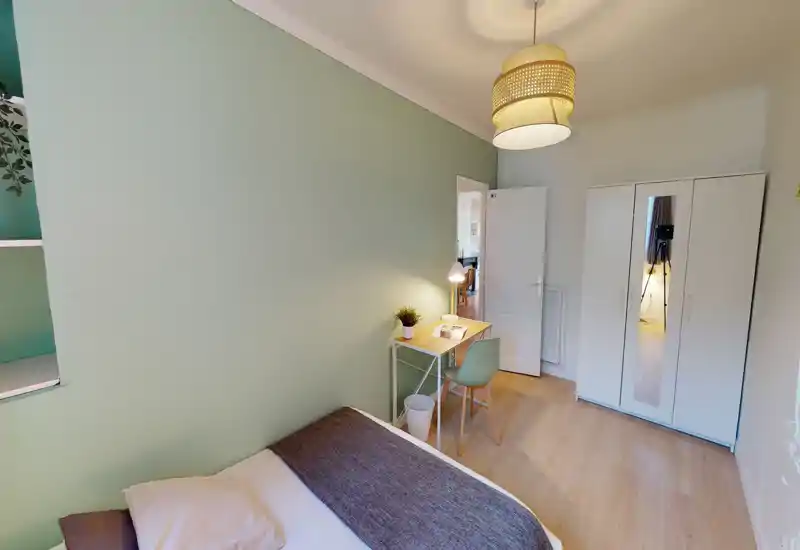Chambre lumineuse et compacte avec un lit simple, une lampe de chevet et un petit bureau contre le mur ; parquet clair et armoire blanche pour une allure moderne et soignée.