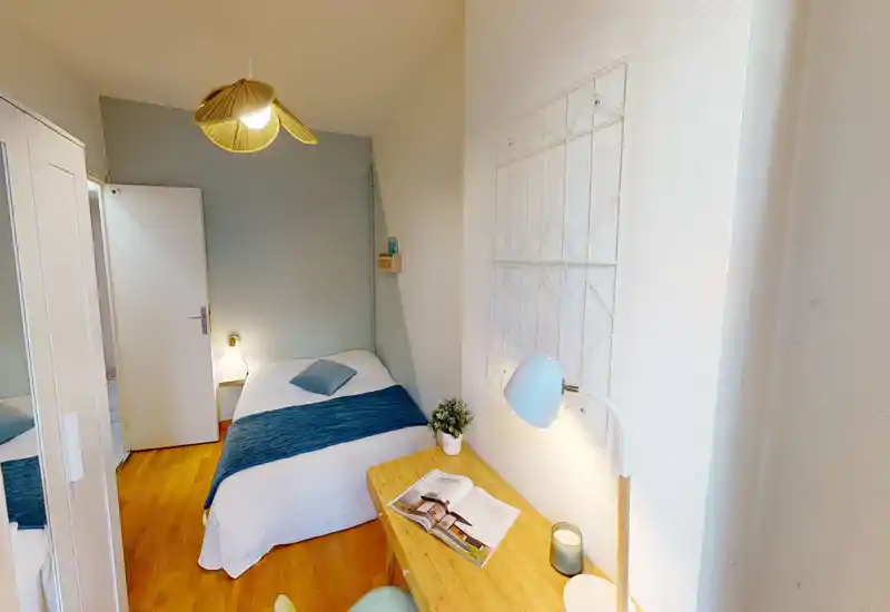 Bright, neatly staged single bedroom with a double bed, desk and cozy accents. The room features a wooden floor, pale blue accent wall and good natural/ambient lighting.