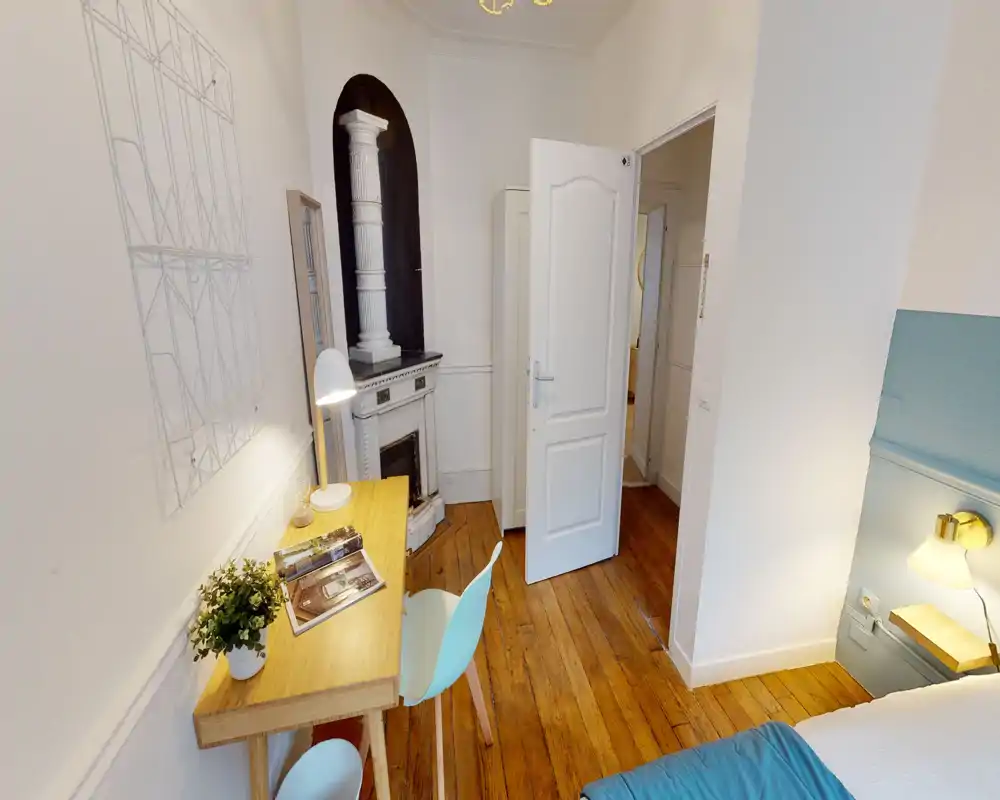 Petit coin chambre élégant avec tête de lit visible, lampe de chevet et bureau en bois près d'une cheminée décorative — lumineux et accueillant.