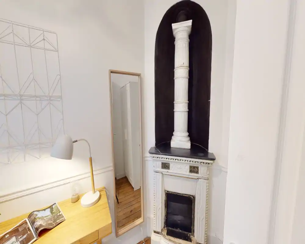 Coin salon avec une cheminée décorative en fonte, un bureau en bois avec lampe et une grande glace — lumineux, soigné et idéal comme coin lecture ou travail.