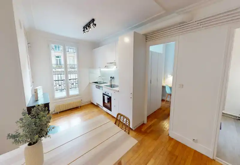 Bright, compact kitchen with integrated white cabinetry, oven and sink, plus a small dining table by the window—ideal for a city apartment.