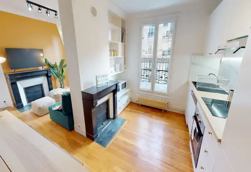 Bright, compact open-plan kitchen with white cabinets, induction hob and oven, overlooking a window and flowing into a cozy living area — ideal for a city apartment.