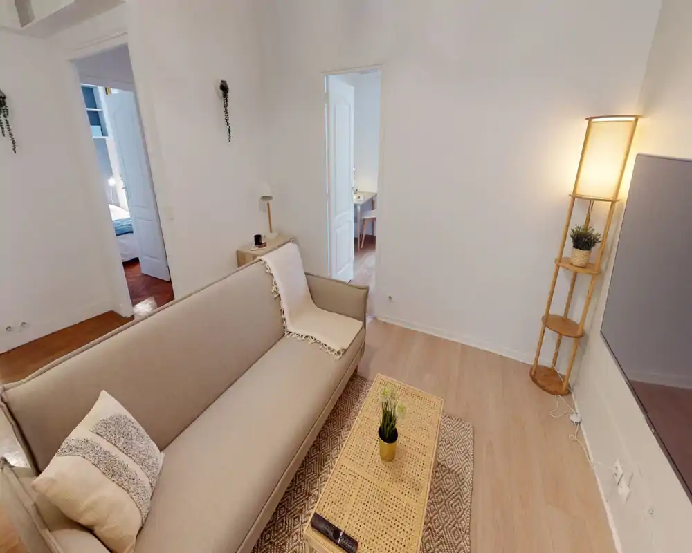 Salon lumineux et chaleureux avec canapé neutre, table basse tressée et lampe sur pied au ton chaud — décor soigné et confortable.