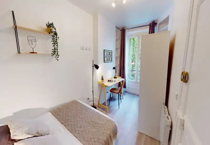 Bright, modern bedroom with a comfortable double bed, woven throw and pillows, plus a small desk by the window offering natural light — ideal for work or relaxation.