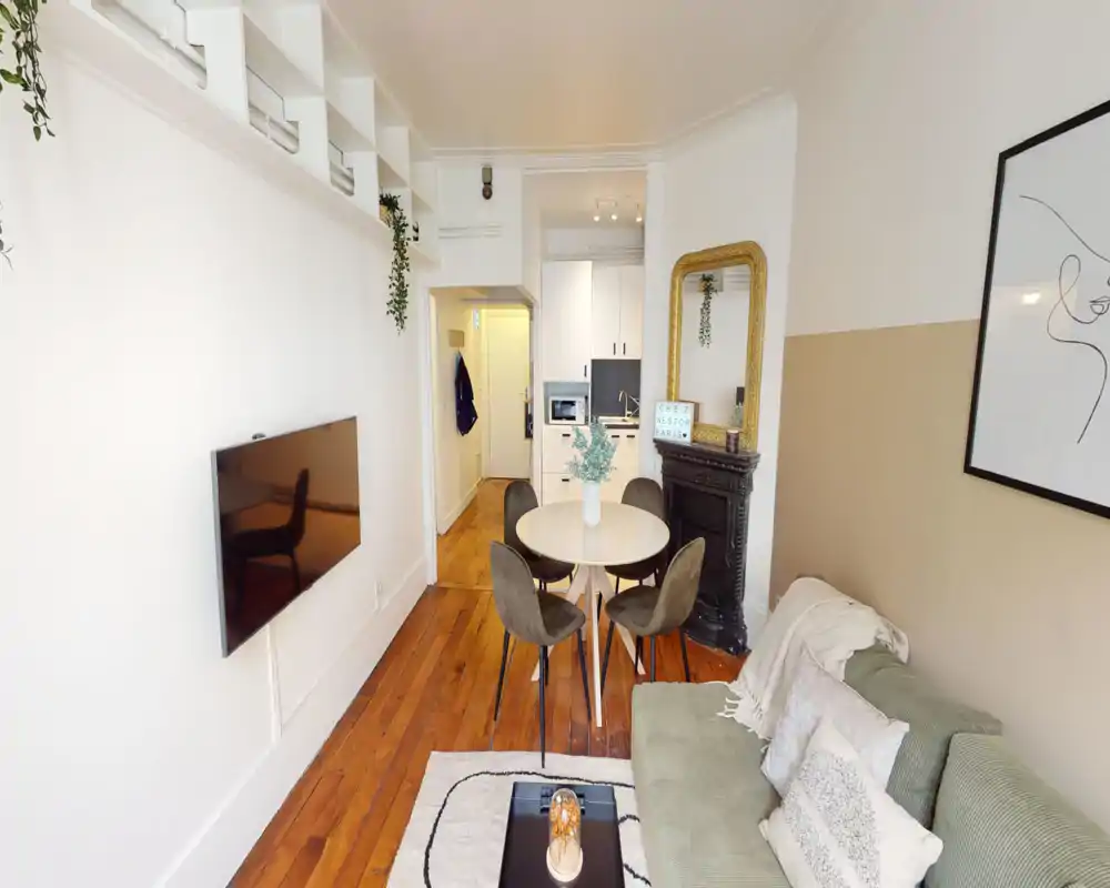 Bright and stylish living area with a comfortable sofa, round dining table and wall-mounted TV — ideal for relaxing or dining in a compact, well-decorated studio.