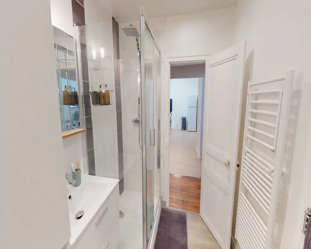 Modern, bright bathroom featuring a glass-enclosed shower, white vanity with sink, and heated towel rail. Clean lines and neutral tiles create a fresh, minimalist feel ideal for a rental listing.