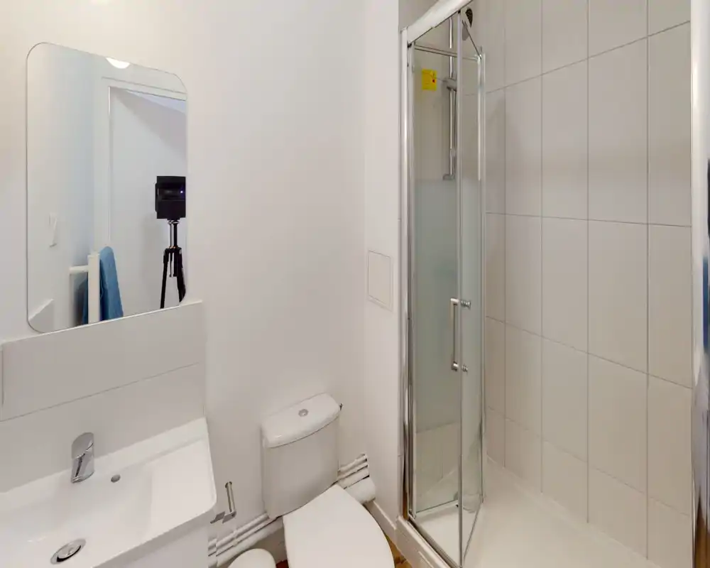 Salle de bains moderne et compacte avec cabine de douche, toilette et lavabo ; carrelage blanc et sanitaires propres pour un rendu lumineux et minimaliste.