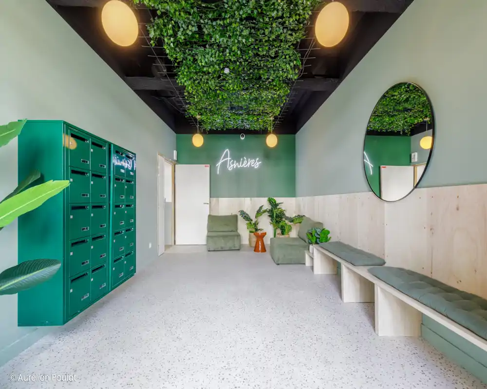 Couloir d'entrée avec miroirs décoratifs et plantes ; l'image est fortement corrompue mais laisse voir un hall avec sièges et casiers.
