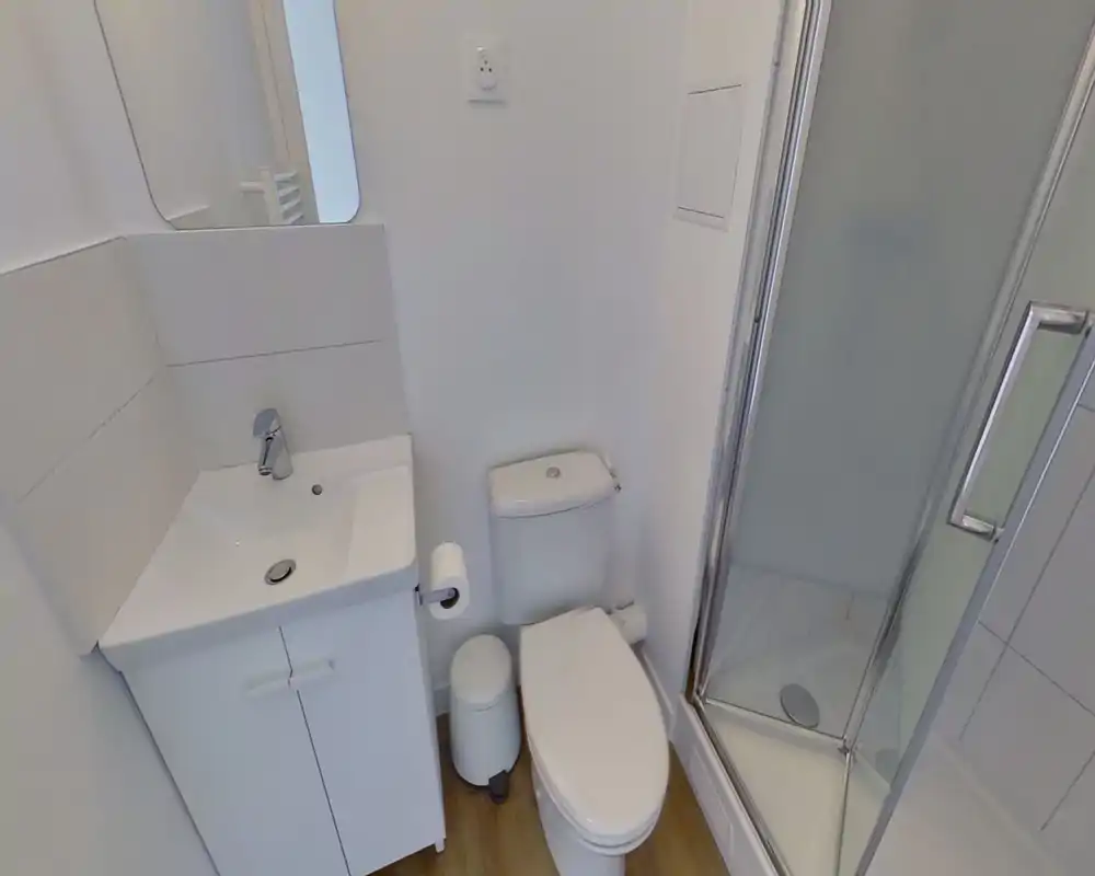 Compact, modern bathroom with a sink and cabinet, toilet and a corner glass shower. Clean white finishes and good natural lighting create a fresh, functional space.
