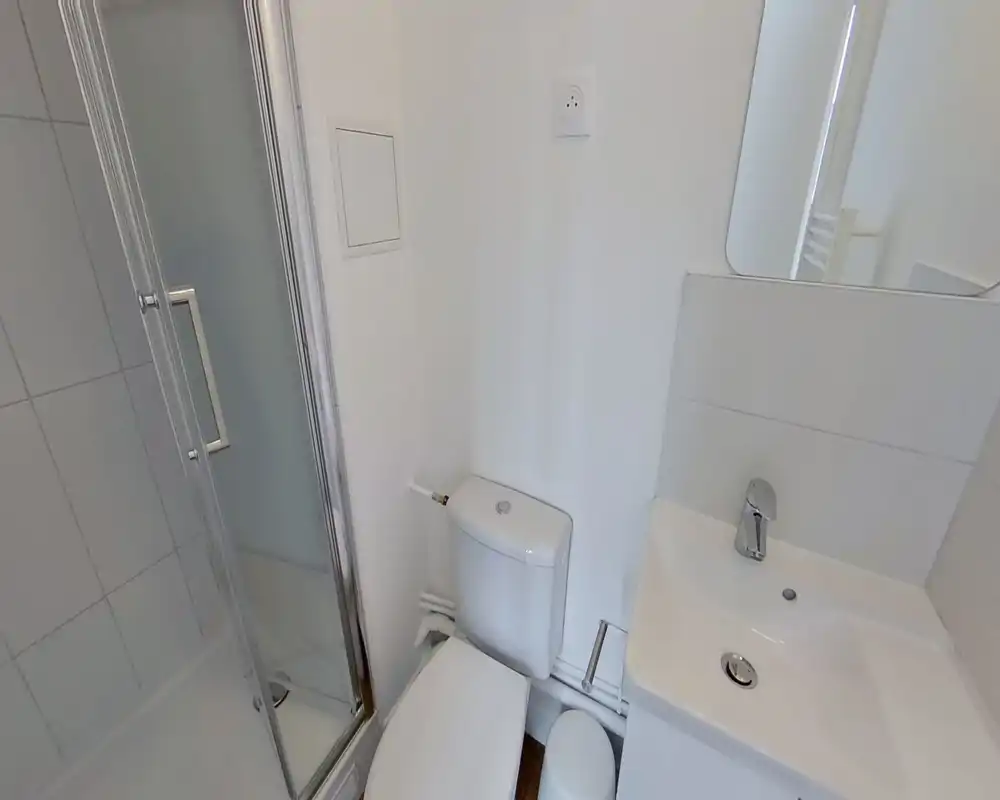Compact modern bathroom with a shower enclosure, toilet and sink; clean white tiles and chrome fixtures create a bright, minimalist feel.