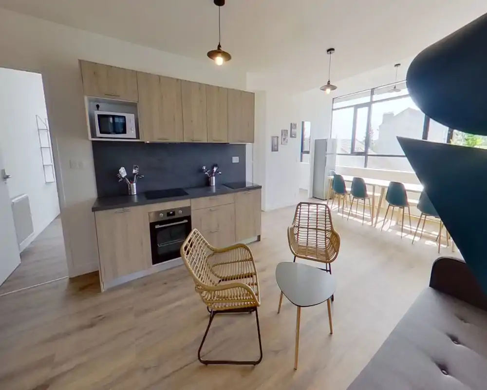 Bright, modern open-plan living area with a kitchenette, rattan lounge chairs and a long dining bar by large windows that flood the space with natural light.