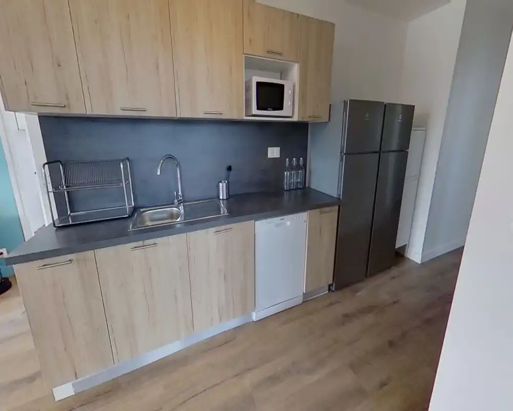 Modern fitted kitchen with wood-effect cabinets, integrated sink, dishwasher and double fridge. Clean countertop and neutral backsplash create a tidy, functional cooking space.