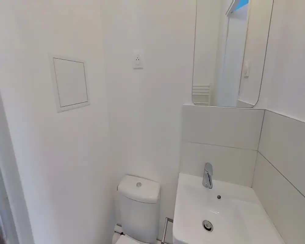 Small modern bathroom with white tiles, a compact toilet and a sink with chrome faucet. Clean minimalist finish and a wall mirror above the basin.