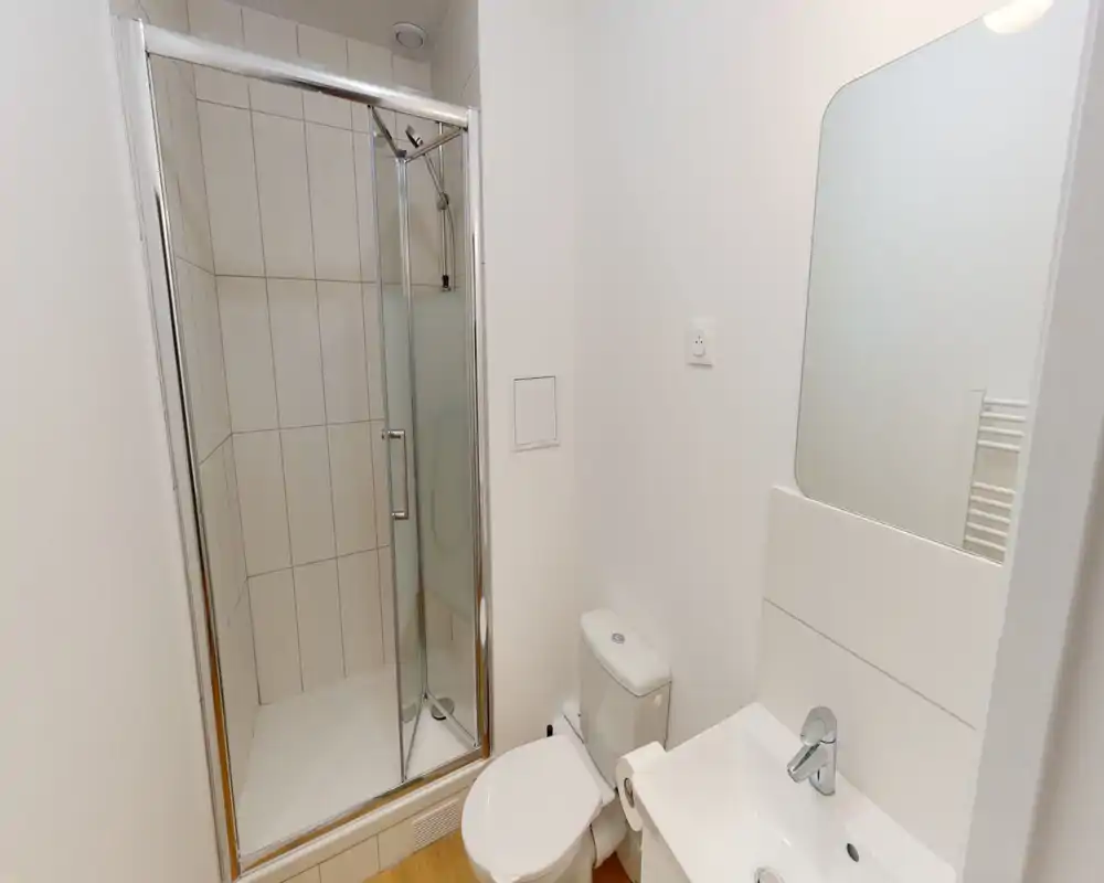 Baño compacto y moderno con ducha alicatada, inodoro y lavabo con espejo. Acabados blancos y estética luminosa y minimalista.