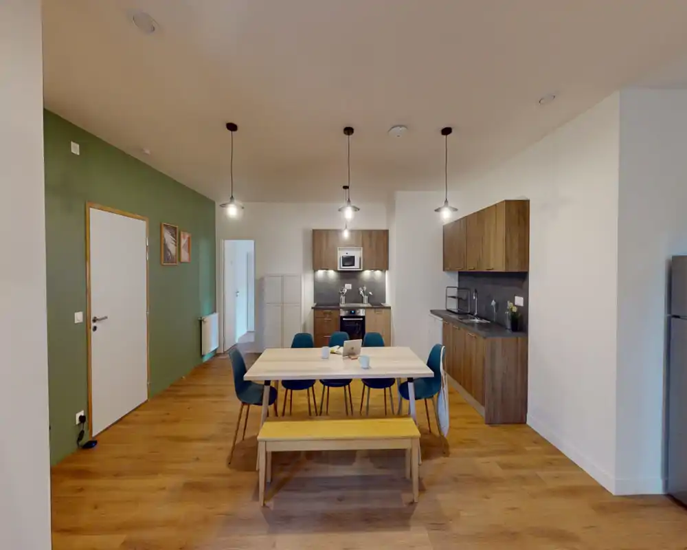 Cocina moderna de concepto abierto con gran mesa de comedor, armarios de madera, horno empotrado y lámparas colgantes: un espacio luminoso y bien decorado ideal para comer en grupo.