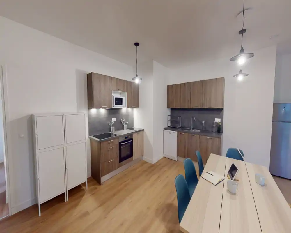 Cocina moderna y luminosa con muebles efecto madera, horno y microondas integrados, zona de fregadero y mesa con sillas — perfecta para cocinar y comer de forma informal.