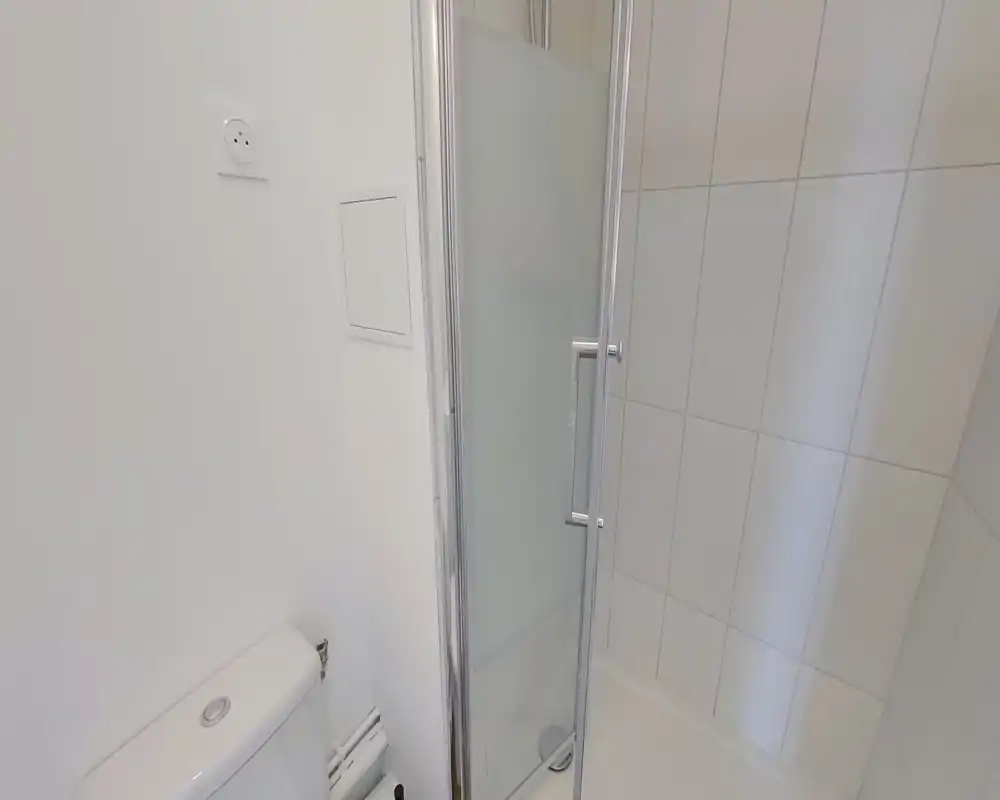 Bagno moderno e compatto con wc, zona doccia piastrellata e porta doccia in vetro con pannello satinato.