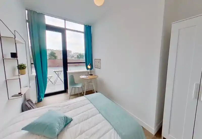 Dormitorio moderno y luminoso con cama cómoda, detalles en turquesa y una pequeña mesa de trabajo junto a una gran ventana con acceso al balcón.