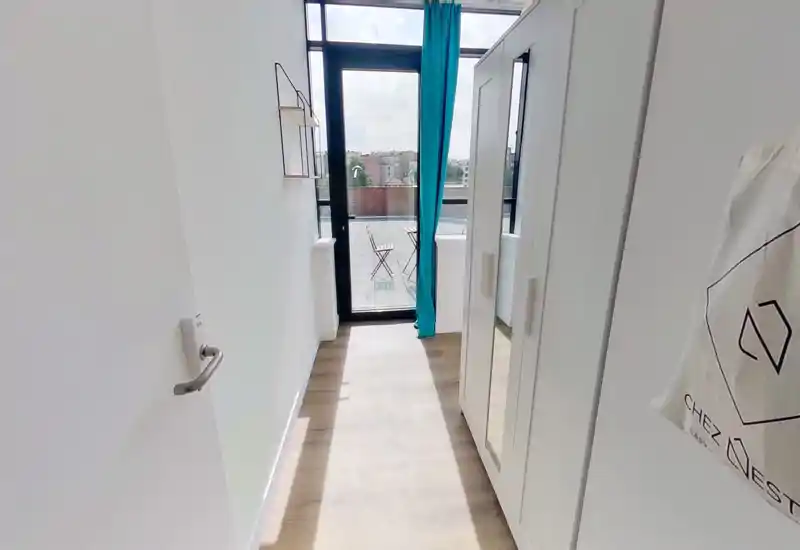 Ingresso/corridoio luminoso e stretto con pavimento in legno, un armadio a destra e una porta vetrata che conduce a un piccolo balcone/terrazza.