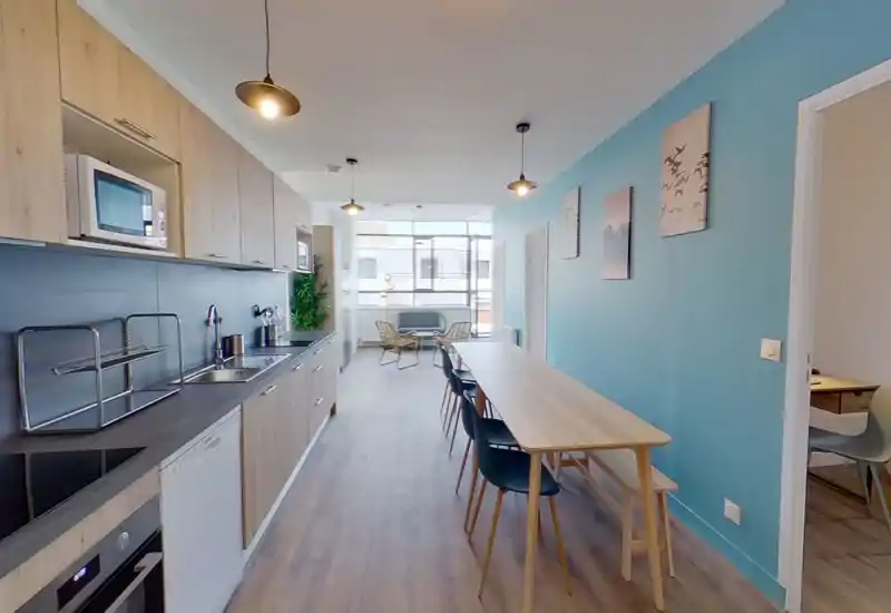 Cucina open space moderna e luminosa con mobili effetto legno, elettrodomestici integrati e un lungo tavolo da pranzo; ampie finestre garantiscono molta luce e un'atmosfera contemporanea.