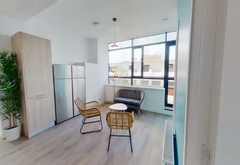 Bright modern living area with a small tufted sofa, two rattan chairs and a coffee table positioned in front of a large window that fills the room with natural light.