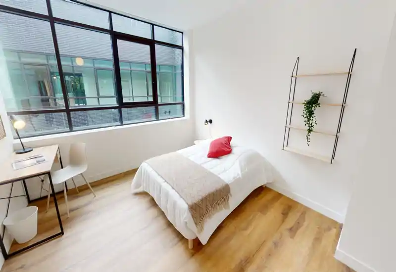 Habitación individual luminosa y minimalista con cama cómoda, escritorio junto a la gran ventana y suelos de madera — ideal para estudiantes o inquilinos solos.