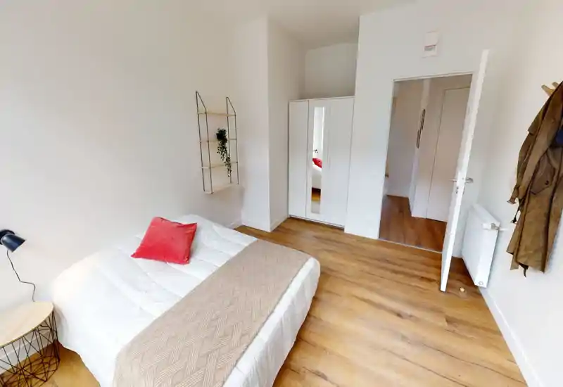 Dormitorio luminoso y sencillo con cama doble, textiles acogedores y un armario. Suelo de madera clara y paredes neutras que crean un ambiente moderno y tranquilo.
