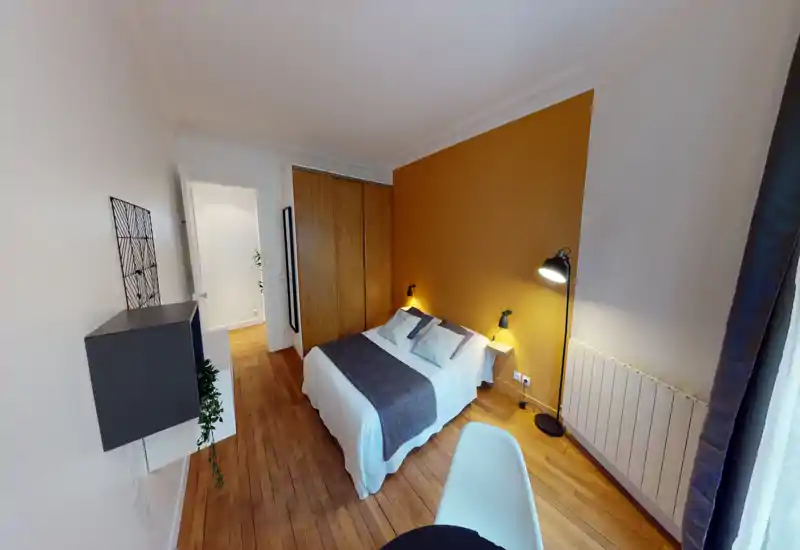 Chambre lumineuse et aménagée avec un lit double, un mur d'accent moutarde, une armoire en bois et des lampes de chevet pour une ambiance chaleureuse.