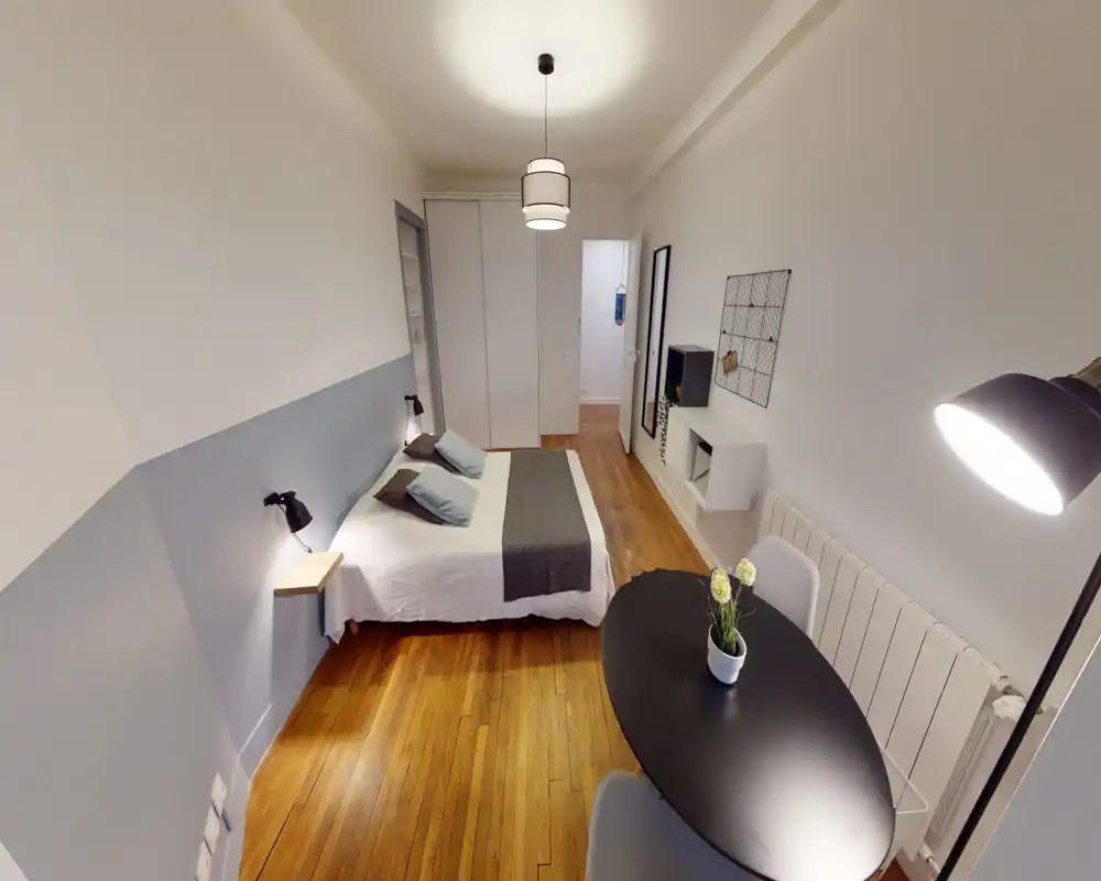 Camera da letto luminosa e di stile con letto matrimoniale, lampade da lettura ai lati, armadio a muro e un piccolo tavolo che può servire da zona pranzo o lavoro. Pavimenti in legno e tessuti morbidi creano un ambiente caldo e accogliente.