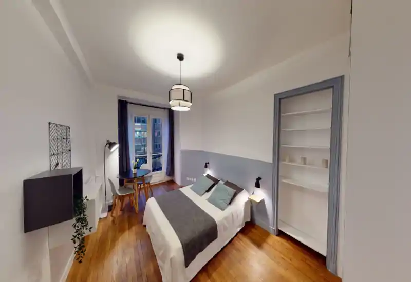 Camera da letto luminosa e ben arredata con letto matrimoniale, lampade da comodino e un piccolo tavolo vicino alla finestra. Linee pulite, parquet e tessili morbidi creano un ambiente accogliente e moderno, perfetto per soggiorni brevi.