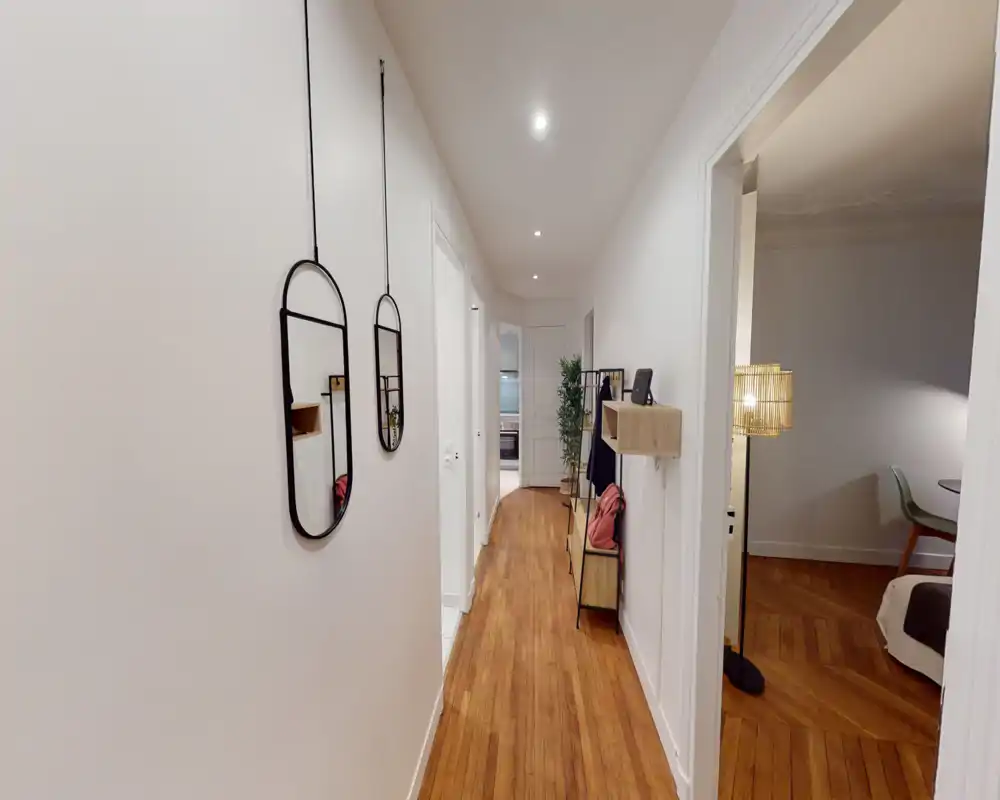 Entrée/couloir lumineux et étroit avec parquet, miroirs suspendus et petit meuble/portemanteau — un espace de transition soigné menant aux autres pièces.