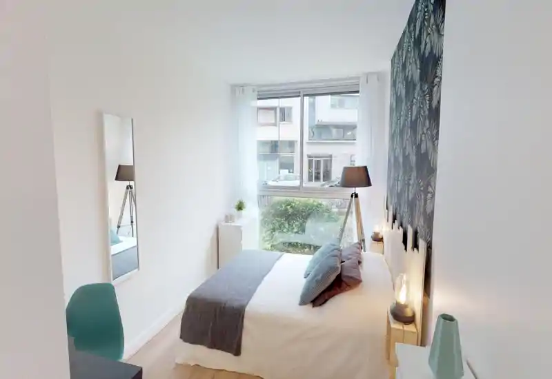 Bright, well-staged bedroom with a double bed, decorative pillows and a cozy throw; large window provides abundant natural light and a pleasant street view.