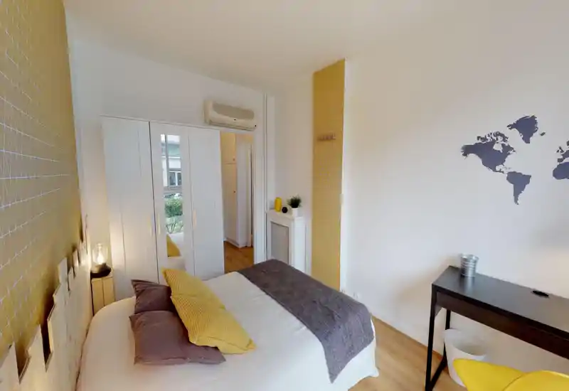 Bright, styled bedroom with a double bed dressed in neutral linens and yellow accents, a mirrored wardrobe, desk and tasteful wall decor — cozy and well-lit for rental photos.