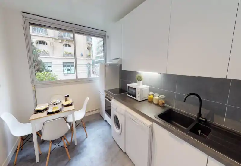 Modern compact kitchen with integrated appliances, a large window and a small dining table for four — bright, well organized and ideal for city apartments.