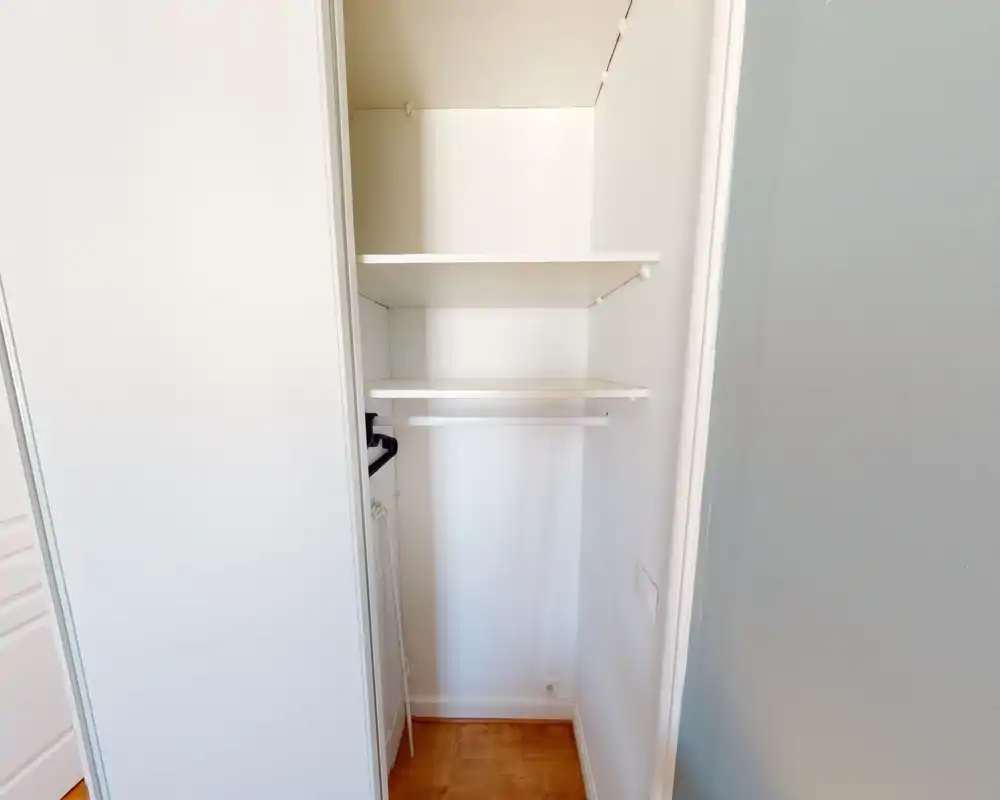 Small built-in closet/entrance storage with two shelves and a hanging rail, bright white finish and wood floor — ideal to show storage space.