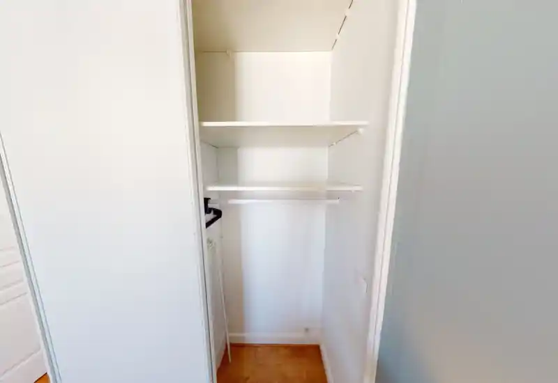 Small built-in closet/entrance storage with two shelves and a hanging rail, bright white finish and wood floor — ideal to show storage space.