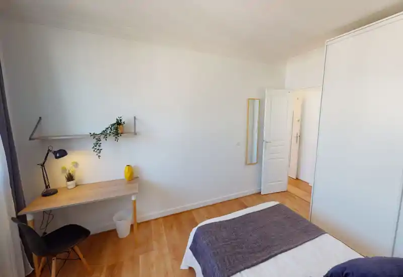 Bright, minimalist bedroom with a visible double bed, wooden floors and a small desk by the window—ideal for a single occupant or couple seeking a clean, calm space.