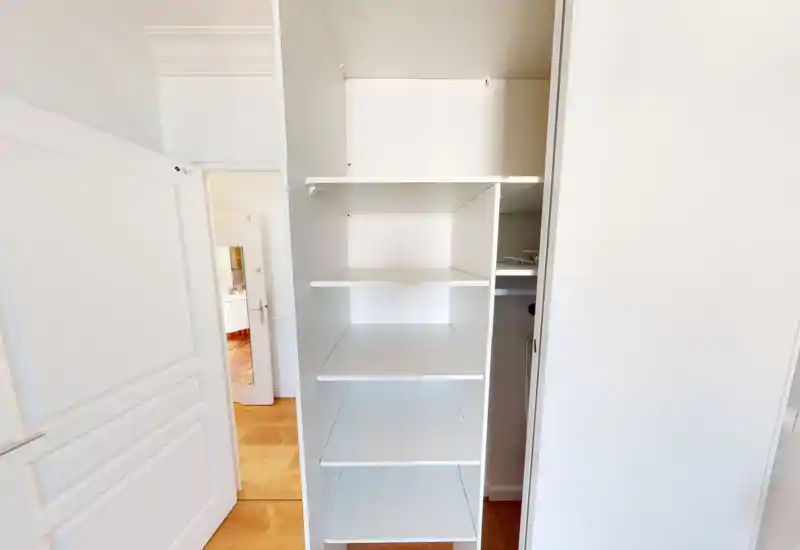 A bright white built-in wardrobe with multiple empty shelves and a view through an open door into another room. The image highlights storage space and clean finishes.