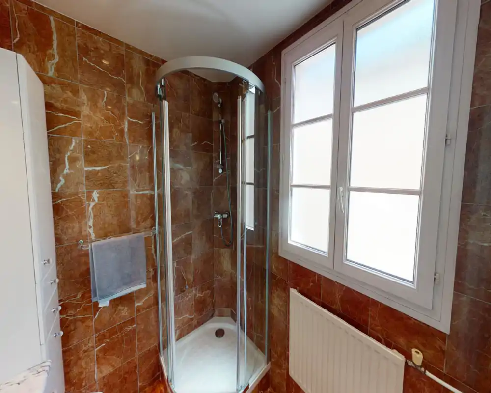 Bright, modern bathroom with a corner glass shower, marble-effect wall tiles and a large frosted window providing natural light.