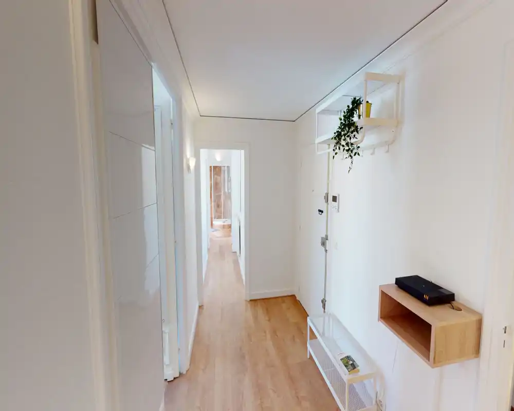 Bright, clean apartment entrance with wood-effect flooring, wall hooks and a small shelf — a welcoming, well-lit hallway connecting to inner rooms.