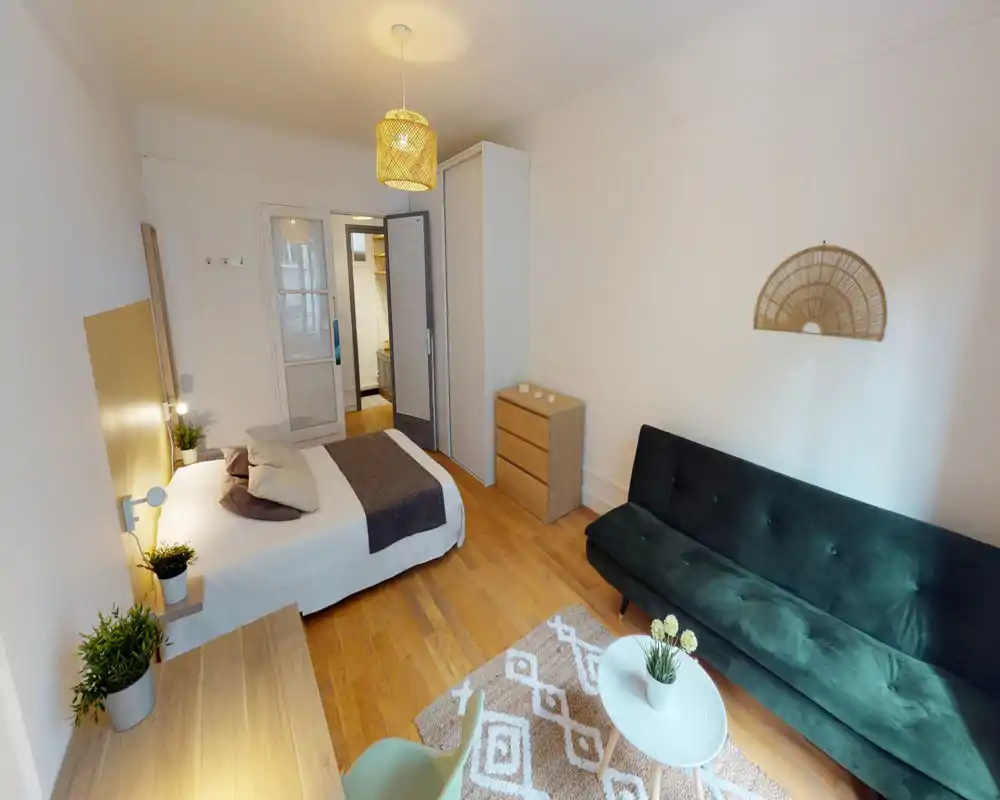 Bright, well-styled bedroom with a full bed, bedside lamps, wooden floors and a dark green sofa — comfortable and neatly staged for short-term rentals.
