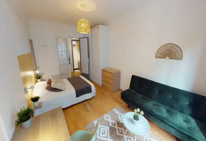 Bright, well-styled bedroom with a full bed, bedside lamps, wooden floors and a dark green sofa — comfortable and neatly staged for short-term rentals.