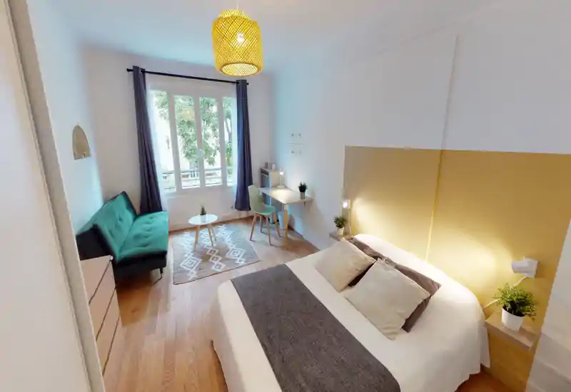 Bright, well-styled bedroom with a comfortable double bed, bedside lamps, a small desk and a green sofa by the window — ideal for a calm, cozy stay.