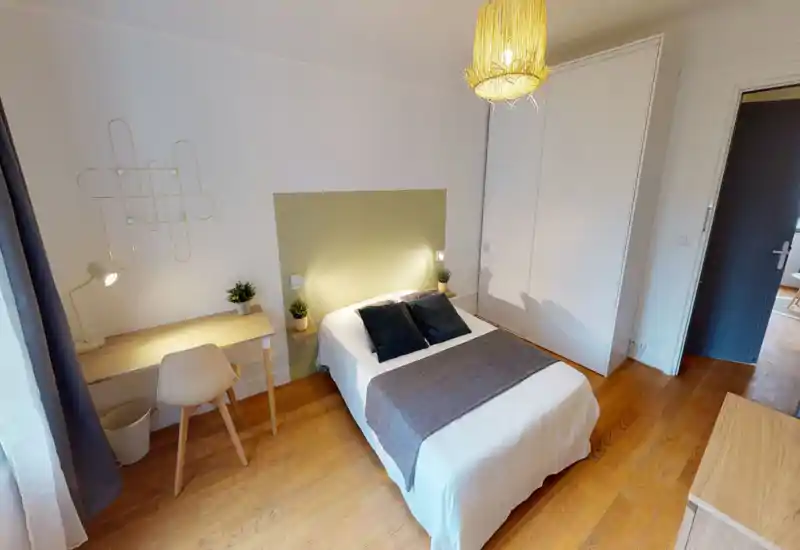 Chambre lumineuse et soignée avec un lit double centré, des textiles chaleureux et un petit espace de travail près de la fenêtre.