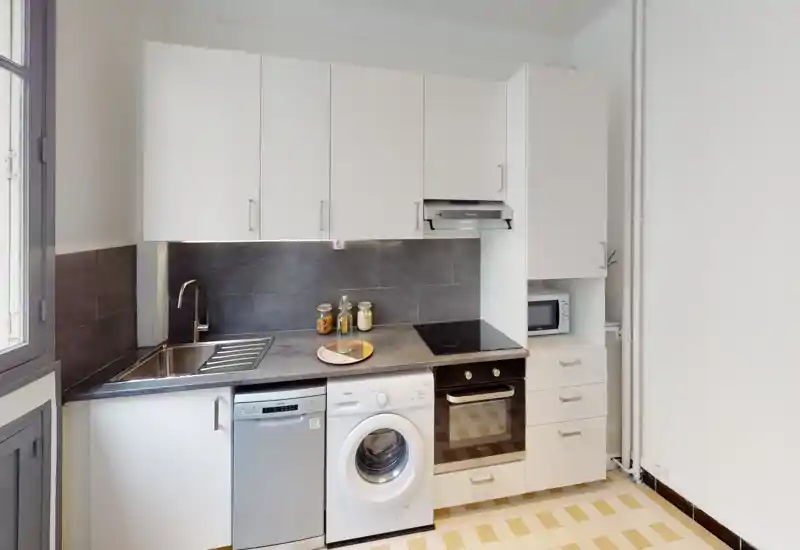 Compact modern kitchen with white cabinets, integrated oven and induction hob, sink, dishwasher and washing machine — bright and neatly presented.