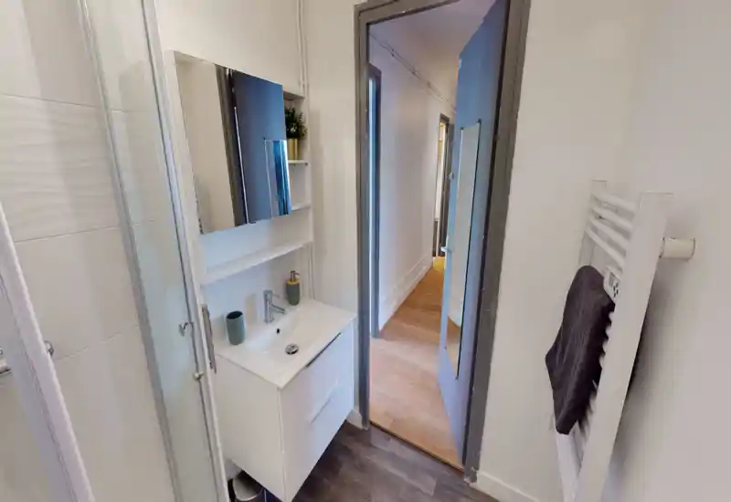 Small modern bathroom with a corner shower, white vanity with sink and mirrored cabinet, and a heated towel rail. Clean lines and bright neutral finishes make it practical for short stays.