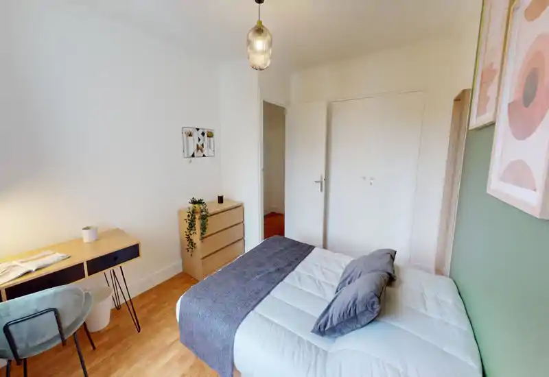 Camera da letto luminosa e ben allestita con letto matrimoniale, cuscini morbidi e plaid decorativo. Pavimento in legno, scrivania e cassettiera rendono l’ambiente accogliente e funzionale per affitti brevi.