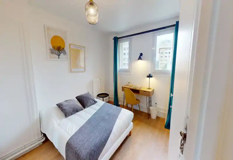 Chambre lumineuse et bien aménagée avec un lit double, des textiles confortables et un petit bureau près de la fenêtre — parfaite pour se détendre et travailler.